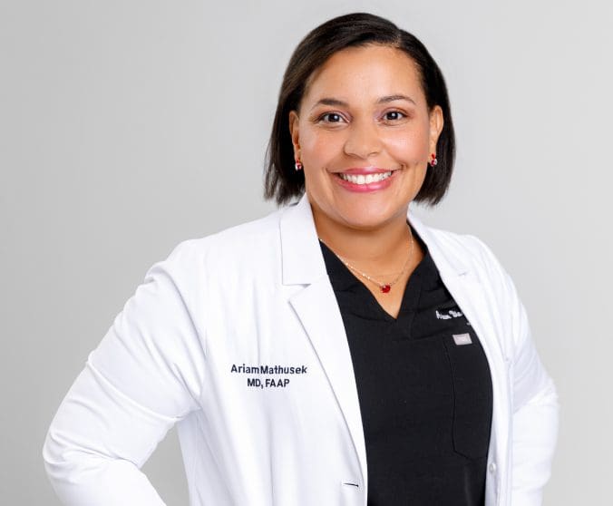 A woman in white lab coat standing next to wall.